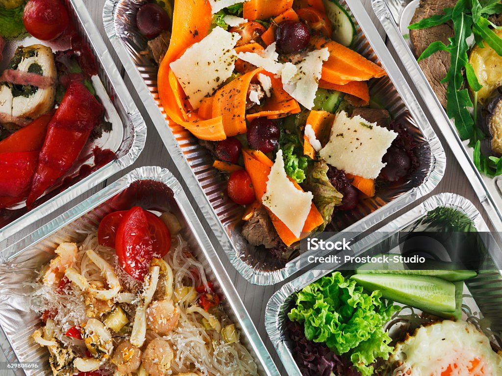 Healthy food take away, top view at wood background Healthy food background. Take away of natural organic food in foil boxes. Fitness nutrition, meat, rice vermicelli, vegetable salads and eggs. Top view, flat lay. Take Out Food Stock Photo