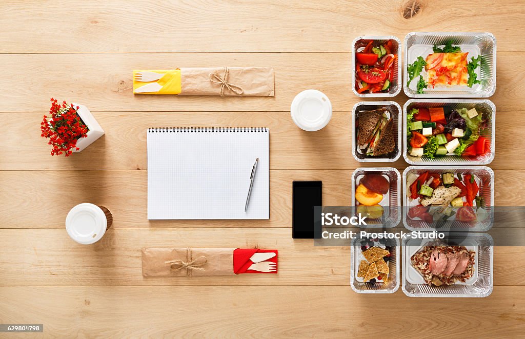 Healthy food take away in boxes, top view at wood Healthy nutrition plan. Fresh daily meals delivery. Restaurant food for two, vegetable, meat and fruits in foil boxes, coffee, tablet and mobile. Top view, flat lay on wood with copy space Planning Stock Photo