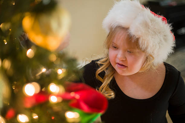 A stock photo of a 10 year old Down syndrome Girl looking at a Christmas Tree whilst wearing a Santa hat. Photographed using the Canon EOS 1DX Mark II