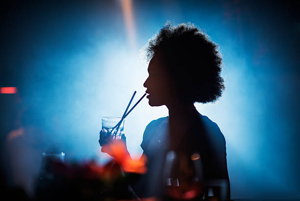 Woman drinking in the bar Mixed race woman having a cocktail in the bar at night out. Bright light is coming from behind. entertainment club stock pictures, royalty-free photos & images