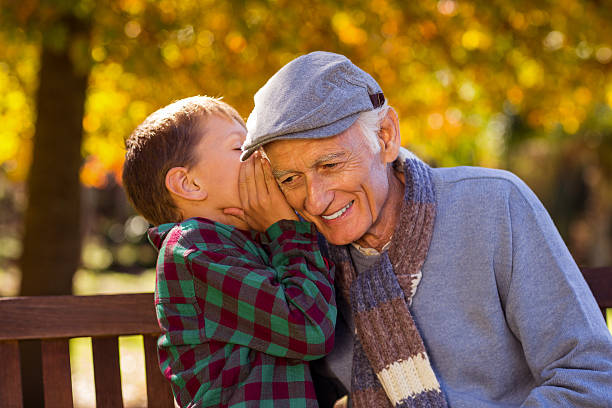 nipote che sussurra al nonno - whispering grandparent child grandfather foto e immagini stock