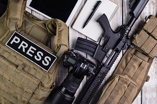 Body armor  for journalist,DSLR camera,rifle,notebook,army belt and tablet touch computer on wooden table.Top view