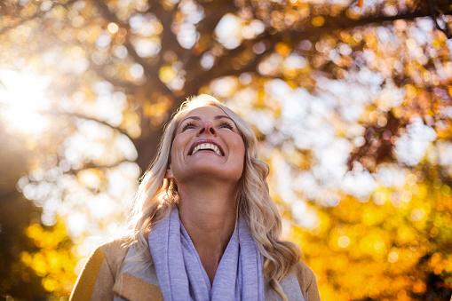 Smiling woman looking up against trees at park during autumn