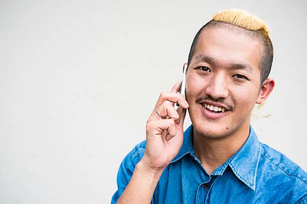 Front view of young man with Iroquois hair style talking on mobile against white wall with lot of copy space.