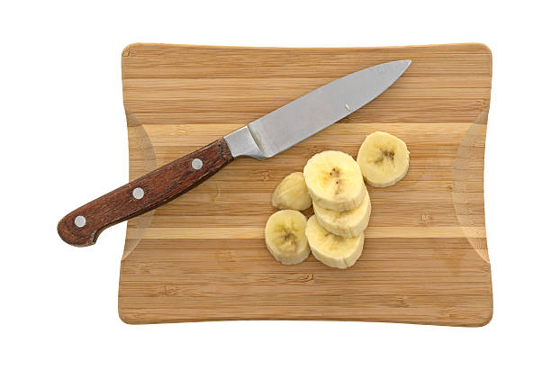 Top view of sliced bananas on a wood cutting board with a knife isolated on a white background.