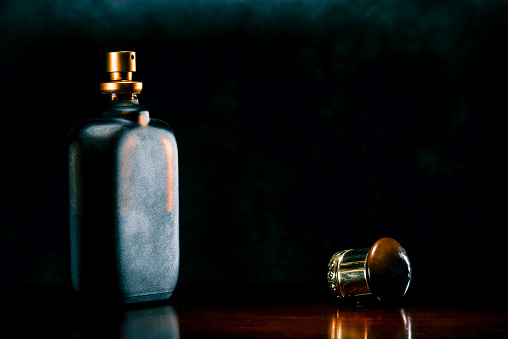 Flat scent bottle of frosted glass on a dark surface of the noble wood.