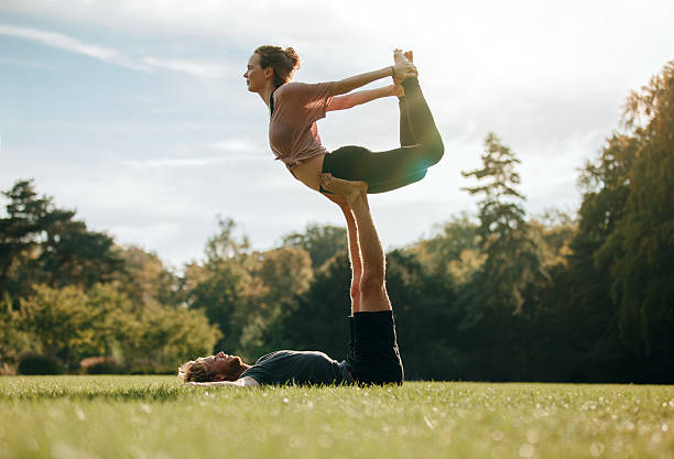 Fit young couple doing acro yoga Fit young couple doing acro yoga. Man lying on grass and balancing woman in his feet. Acrobatic balance in park. acroyoga stock pictures, royalty-free photos & images