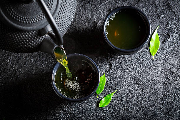 köstlicher grüner tee mit teekanne und tasse auf schwarzem felsen - chinese tea stock-fotos und bilder