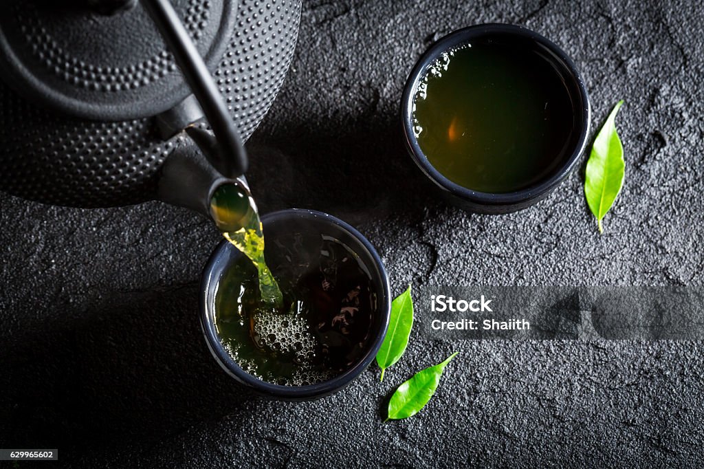 Delicious green tea with teapot and cup on black rock Tea Crop Stock Photo