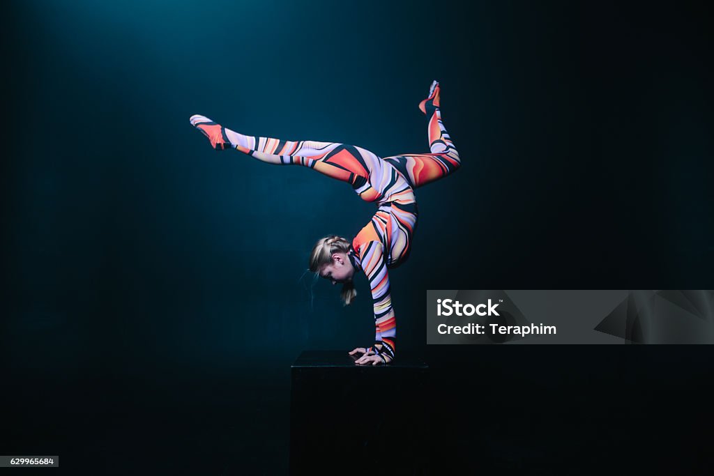 Flexible circus acrobat doing equilibre balance handstand on a cube. Young flexible blonde circus acrobat posing in studio in costume. Doing equilibre balance handstand on a cube. Copy space text. Gymnastics Stock Photo