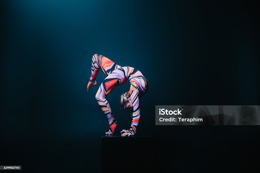 Flexible circus acrobat doing equilibre balance handstand on a cube. Young flexible blonde circus acrobat posing in studio in costume. Doing equilibre balance handstand on a cube. Copy space text. Circus Stock Photo