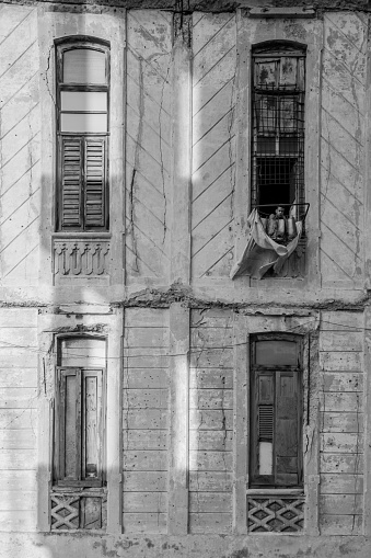 Havana, Cuba - October 10, 2016: Old Havana quarter street facade in the evening. Rough facades of old colonial apartment buildings. Man looking out the window from one of the apartments. Typical scene all around old Havana, where ever you see old buildings with people still living inside. Variety of colours and styles. Beauty of old architecture neglected over many years with out upkeep. 
