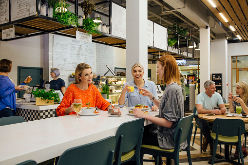 Three women are sitting at a table in a health cafe. They are eating organic, vegan meals while talking and laughing.