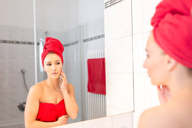 молодая женщина в ванной принимает лосьон о ее лице - finalise сто�ковые фото и изображения