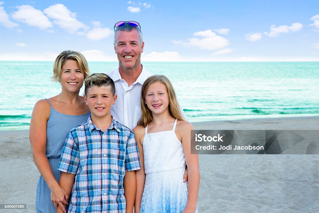 Series:Portrait of real caucasian family of four on beautiful beach An attractive caucasian family consisting of a mother, father, young son and daughter are on the beach in coordinating blue clothes having their picture taken with the ocean behind them. Shot taken with Canon 5D Mark lll. Accuracy Stock Photo