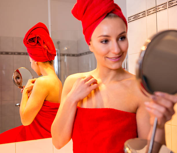 молодая женщина в ванной принимает лосьон о ее лице - finalise стоковые фото и изображения