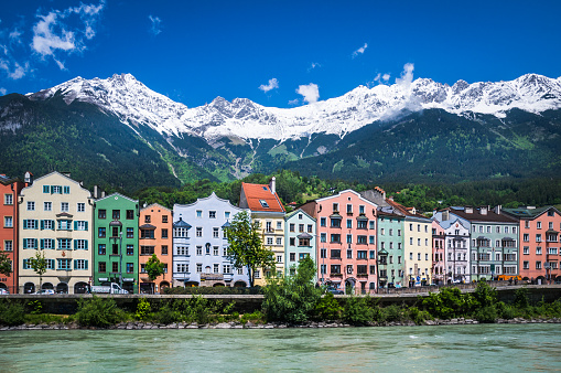  Innsbruck, Austria - May 25, 2016: The colorful facades of several hotels, cafes, restaurants and other shops face the River Inn and have the snow capped Alps in their backyard.