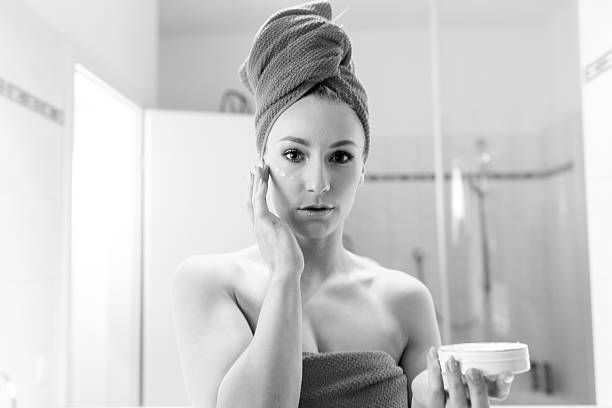 молодая женщина в ванной принимает лосьон о ее лице - finalise стоковые фото и изображения