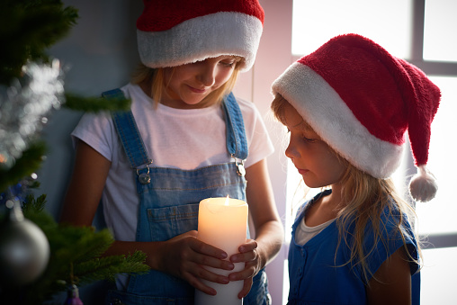 Elder sister holding burning candle, two girls looking at flame