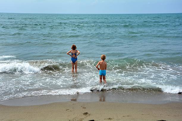 istock Two children  stand in the water on the beach 630041744