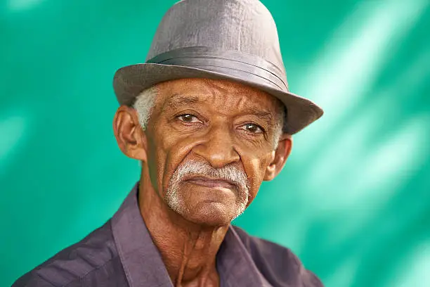 Real Cuban people and feelings, portrait of sad senior hispanic man looking at camera. Worried old latino grandfather with mustache and hat from Havana, Cuba