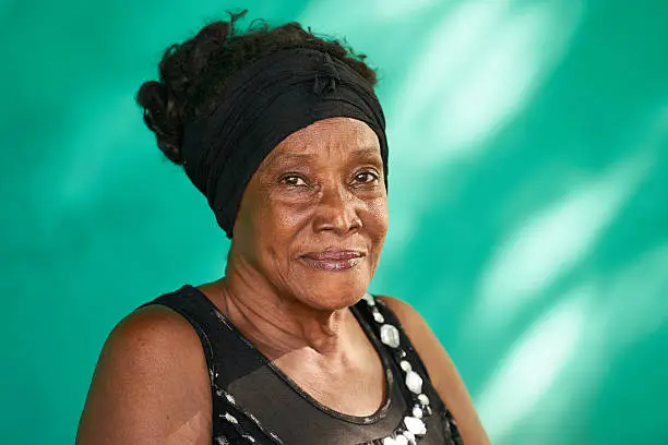 Old Cuban people and emotions, portrait of happy senior african american lady looking at camera. Copy space on green wall in background.