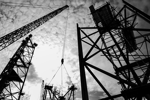 Silhouette black and white shot of construction sites with ringer cranes and scaffolding.