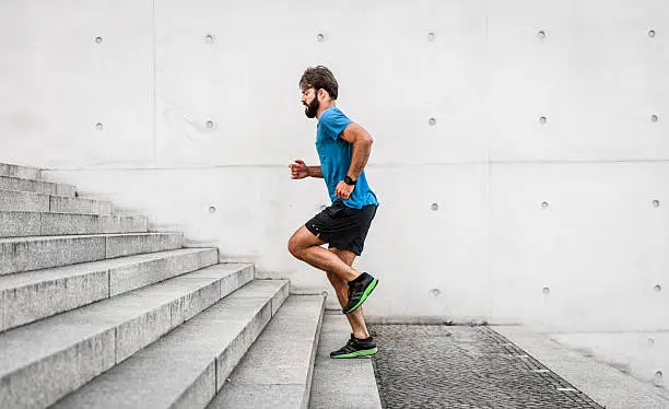 Photo of sporty man running up steps in urban setting
