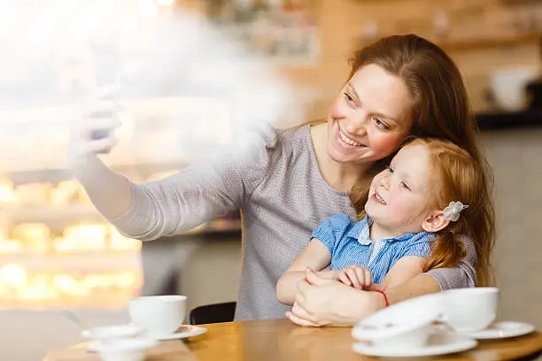 Woman making selfie with her daughter at tea-break in cafe
