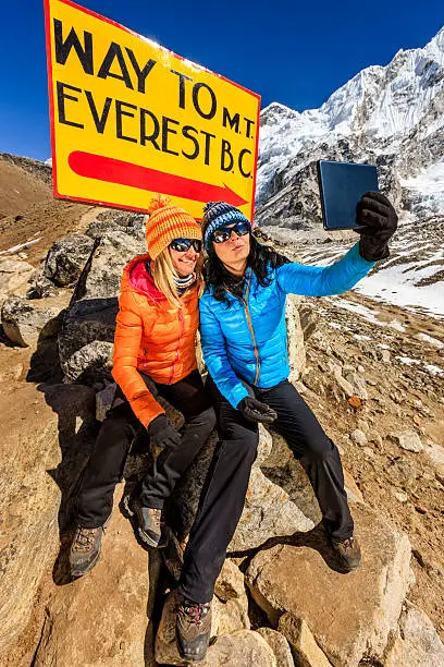 Young women taking selfie in Himalayas, next to the signpost "Way to Mount Everest Base Camp" . One of them, wearing blue jacket, is holding a digital tablet and the second woman is wearing orange jacket. Mount Everest National Park. This is the highest national park in the world, with the entire park located above 3,000 m ( 9,700 ft). This park includes three peaks higher than 8,000 m, including Mt Everest. Therefore, most of the park area is very rugged and steep, with its terrain cut by deep rivers and glaciers. Unlike other parks in the plain areas, this park can be divided into four climate zones because of the rising altitude. The climatic zones include a forested lower zone, a zone of alpine scrub, the upper alpine zone which includes upper limit of vegetation growth, and the Arctic zone where no plants can grow. The types of plants and animals that are found in the park depend on the altitude.http://bhphoto.pl/IS/nepal_380.jpg