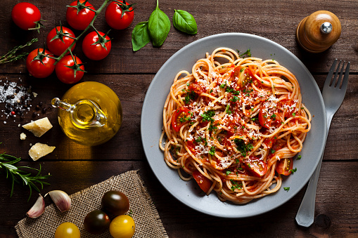 Pasta with tomato sauce shot from above on rustic wood table. Some ingredients for cooking pasta like tomatoes, olive oil, basil, parmesan cheese and a pepper mill are around the plate. DSRL low key studio photo taken with Canon EOS 5D Mk II and Canon EF 100mm f/2.8L Macro IS USM