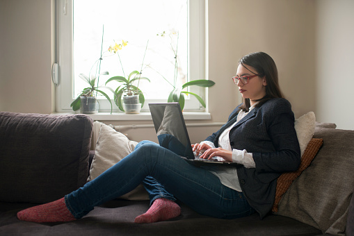 Beautiful young businesswoman sitting casually on the couch and working on the laptop
