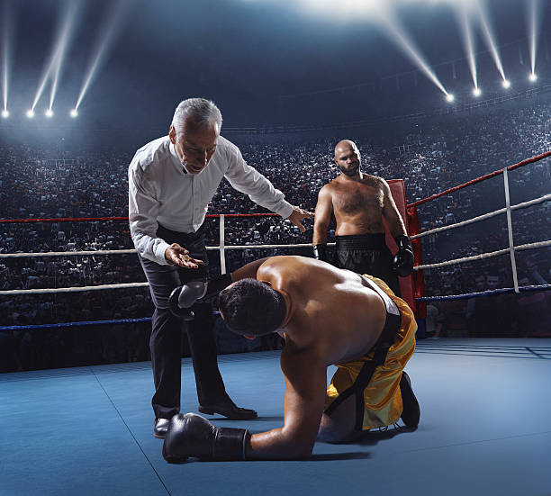 Boxing: Winner boxer A picture of a boxer who made knock out to the opposite one. The other sportsman is on the floor. Referee counts. Sportsmen are on boxing ring with bleachers full of people boxing referee stock pictures, royalty-free photos & images