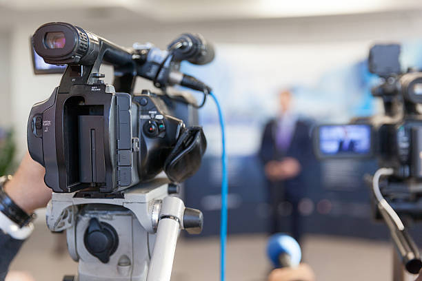 istock Video camera in focus, blurred spokesman in background 634574504