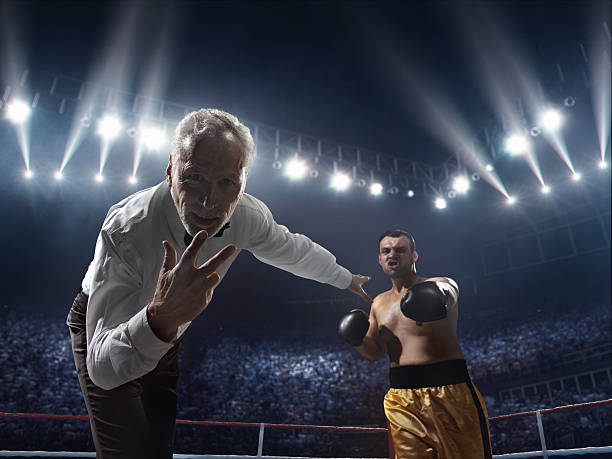 Boxing: Winner boxer A picture of a boxer who made knock out to the opposite one. Referee counts. Sportsmen are on boxing ring with bleachers full of people boxing referee stock pictures, royalty-free photos & images