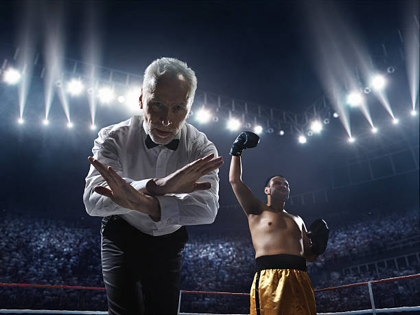 Boxing: Winner boxer A picture of a boxer who made knock out to the opposite one. Referee counts. Sportsmen are on boxing ring with bleachers full of people boxing referee stock pictures, royalty-free photos & images