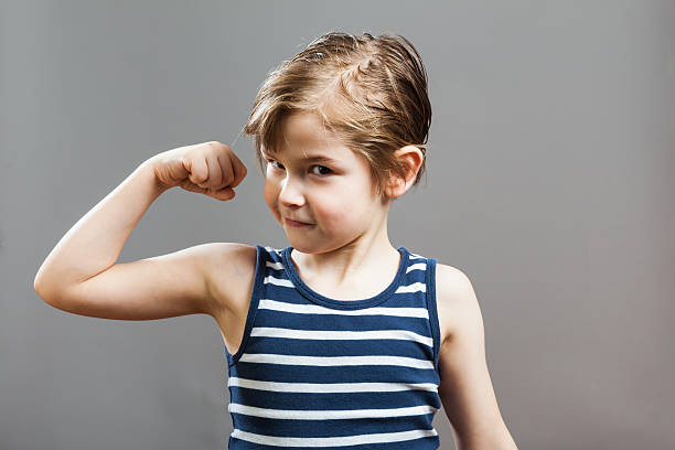 istock Portrait Of Boy Flexing Muscles Against Gray Background 635101265
