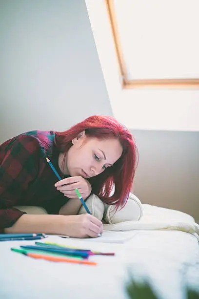 Young beautiful woman lying in her bed, colorful crayons lying next to her