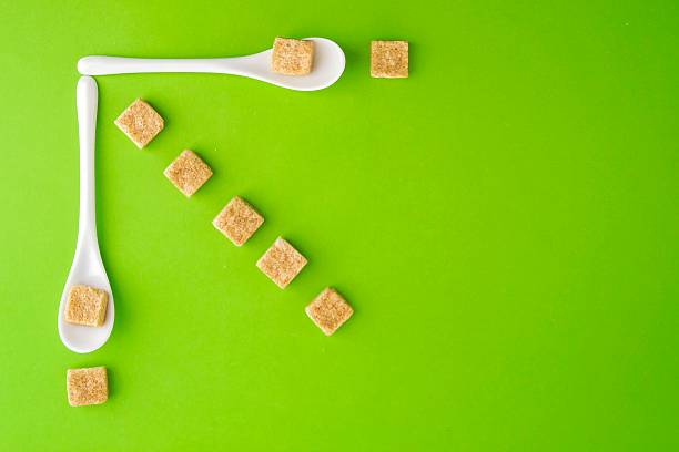 istock Brown sugar cubes and white spoons on greenery background arringed 635678588