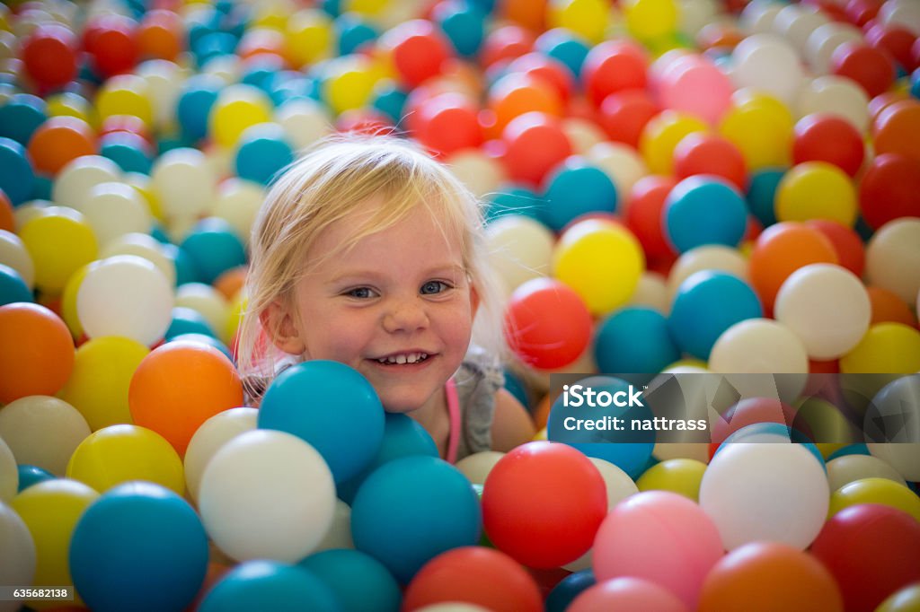 Happy blond girl plays in a ball pool A little blond girls plays in a ball pool full of multi colored balls. She is excited and happy Ball Pool Stock Photo