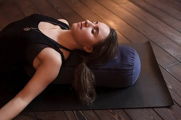 Woman resting after a yoga class in shavasana. Under back her bolster  for spine therapy