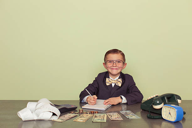Young Boy Accountant Records Taxes to be Paid A young boy accountant and financial advisor with US dollars ready to do business and count your taxes. He is smiling while holding a pen and ready to help your business. Dressed in business suit and bow tie. Retro styled. bringing home the bacon stock pictures, royalty-free photos & images
