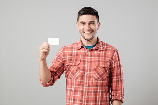 Young man holding and showing blank business card isolated on gray background