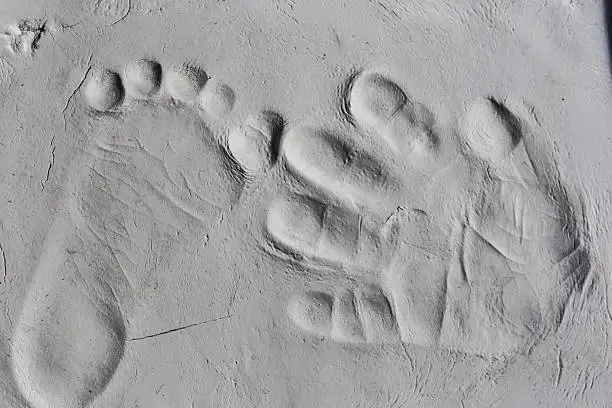 Baby handprint and footprint close up on a scratched bright grey clay