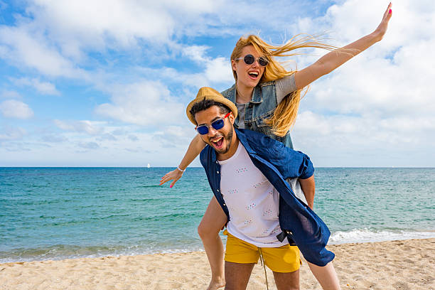 couple piggy backing spinning around by the ocean - group of people women beach community imagens e fotografias de stock