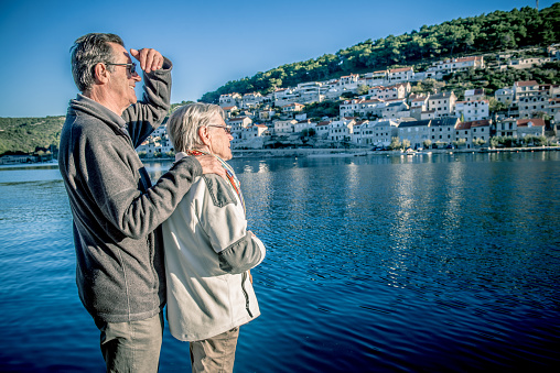 Happy loving senior Caucasian couple standing in the beautiful town Pučišča on the Brač island in the Split-Dalmatia County, Croatia, Mediterranean, Europe. They are embraced and enjoying the sunny autumnal afternoom. Side view. The city of Pučišča is famous because of its white stone buildings and olive oil, vine and figs production in the surroundings. Nikon D800, full frame, XXXL