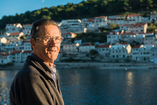 Portrait of a smiling senior Caucasian man in the beautiful town Pučišča on the Brač island in the Split-Dalmatia County, Croatia, Mediterranean, Europe. He is looking at the camera. Sunny autumnal afternoom. The city of Pučišča is famous because of its white stone buildings and olive oil, vine and figs production in the surroundings. Nikon D800, full frame, XXXL