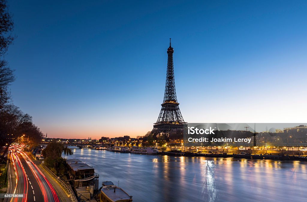 Sunrise at the Eiffel Tower in Paris along the Seine An early morning sunrise takes place behind the majestic Eiffel Tower in the city of Paris in France. Situated near the Seine river, the Eiffel Tower is one of the most important monument in the World. On the left side, cars are on the move and leave some trail lights. Paris - France Stock Photo