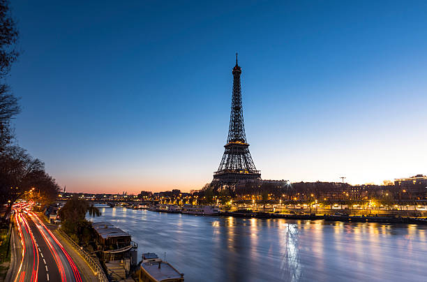 Sunrise at the Eiffel Tower in Paris along the Seine An early morning sunrise takes place behind the majestic Eiffel Tower in the city of Paris in France. Situated near the Seine river, the Eiffel Tower is one of the most important monument in the World. On the left side, cars are on the move and leave some trail lights. paris france stock pictures, royalty-free photos & images