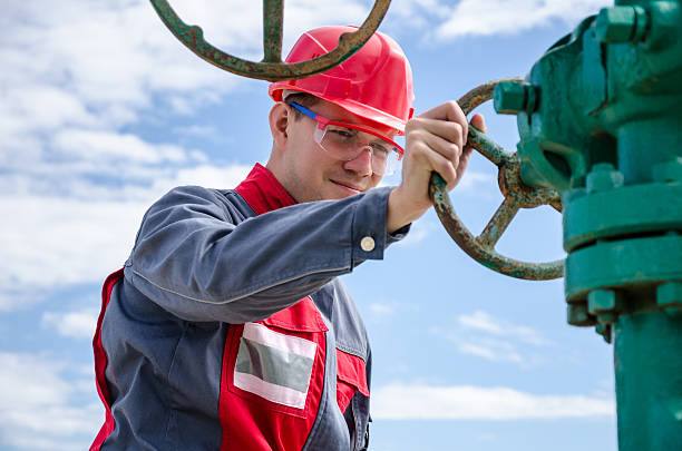 Worker near wellhead valve Worker near wellhead valve wearing red helmet in the oilfield. Oil and gas concept. wellhead stock pictures, royalty-free photos & images